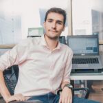 Confident young man in shirt working in modern office with laptop and desk accessories.